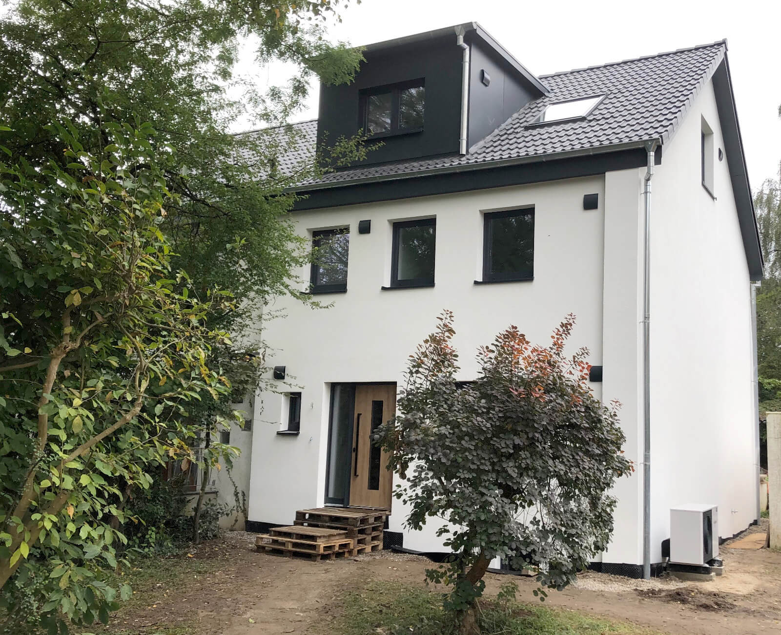 Dasselbe Haus nach der Sanierung: helle Fassade, neue Fenster, Dachgaube und Wärmepumpe